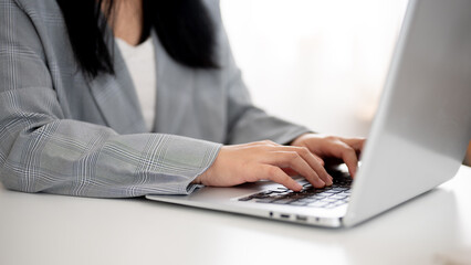 A cropped image of a businesswoman working or browsing on the laptop, working in a modern office.