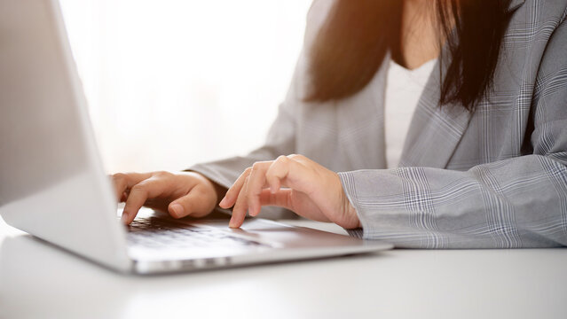 A cropped image of a businesswoman working or browsing on the laptop, working in a modern office.