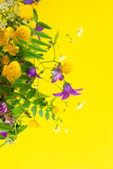 Bright colorful bouquet of small yellow wild flowers, bluebell, tufted vetch, stems on yellow...