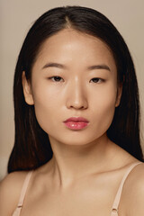Vertical closeup studio portrait of self-confident young adult Asian woman wearing beige bra looking at camera