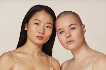 Medium closeup studio portrait of diverse young Asian and Caucasian girl friends wearing neutral...