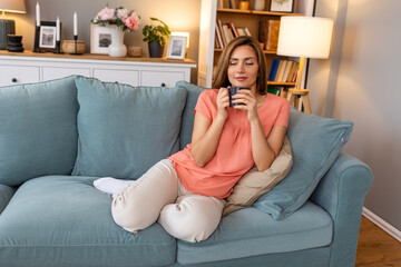 Young happy relaxed woman enjoying quiet moments at home with cup of tea or coffee, smiling female...