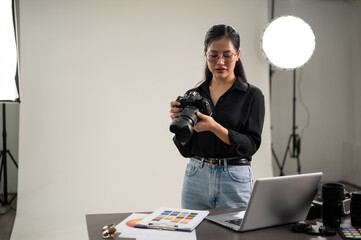 A professional, attractive Asian female photographer is adjusting her DSLR camera for a photoshoot.