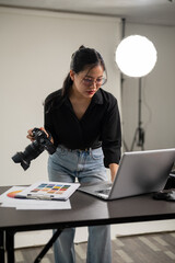 A professional Asian female photographer is checking images on her laptop, working in a studio.
