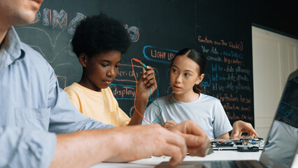 Young student fixing controller while teacher programing engineering code at STEM class. Closeup of...