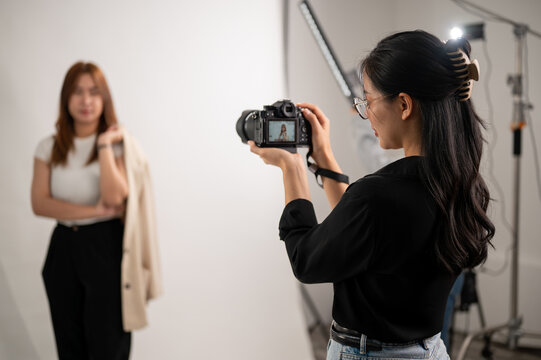 A professional, cool Asian female photographer taking pictures of a model in the studio.