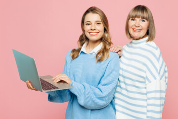 Elder smiling parent mom 50s year old with young adult IT daughter two women together wear blue casual clothes hold use work on laptop pc computer isolated on plain pink background Family day concept - obrazy, fototapety, plakaty