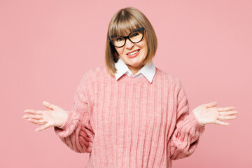 Elderly sad woman 50s years old wears sweater shirt casual clothes glasses shrugging shoulders looking puzzled, have no idea isolated on plain pastel light pink background studio. Lifestyle concept.