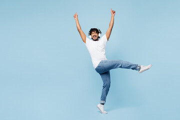 Full body young happy Indian man wear white t-shirt casual clothes listen to music in headphones raise up hands isolated on plain pastel light blue cyan background studio portrait. Lifestyle concept. - 772796537