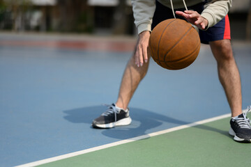 Cropped shot of basketball player bouncing the ball on an outdoor court during a sunny day