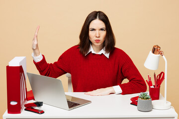 Young sad strict employee business woman she wear red sweater shirt sit work at office desk with pc...