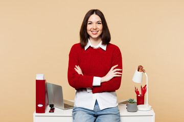 Young fun employee business woman wear red sweater shirt work at office sit on desk with pc laptop...