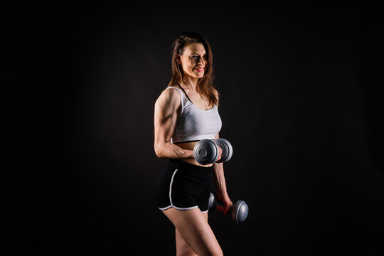 Woman training with dumbbells, pumping up muscles of hands and legs.