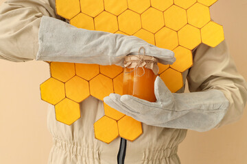 Male beekeeper with paper honeycombs and jar of honey on beige background, closeup