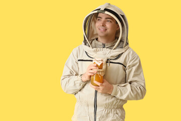 Male beekeeper with jars of honey on yellow background
