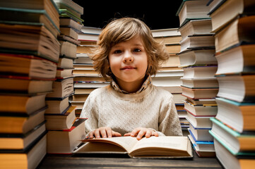 Handsome little child flips through book pages in library. Elementary school boy