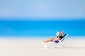 Miniature people , a woman relaxing on a deck chair and reading a book