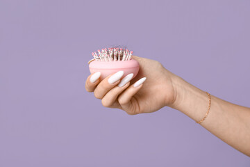 Young woman holding brush with fallen down hair on lilac background, closeup