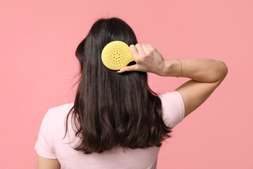 Young woman brushing her hair on pink background, back view - obrazy, fototapety, plakaty
