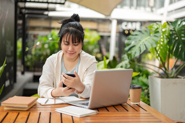 A woman is using her smartphone, checking messages while working remotely at an outdoor space.