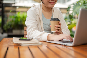 A woman working remotely at an outdoor space, sipping coffee and working on her laptop computer.