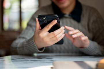 A cropped image of an Asian woman using her smartphone at a table indoors, checking messages
