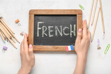 Female hands, chalkboard with word FRENCH and stationery on light background, closeup