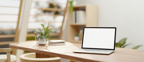 A white-screen laptop mockup on a wooden dining table in a neutral contemporary dining room. - obrazy, fototapety, plakaty