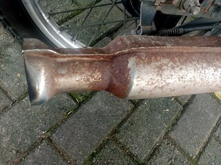 Close up of the rusty exhaust of a motorcycle with the paving block floor in the background