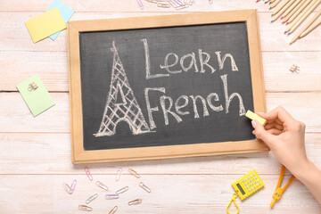 Female hand, chalkboard with text LEARN FRENCH and different stationery on light wooden background