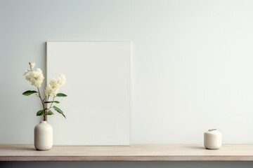 A white vase with flowers sits on a shelf next to a white frame