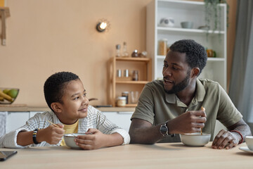 Front view portrait of African American father and son enjoying breakfast together at kitchen table...