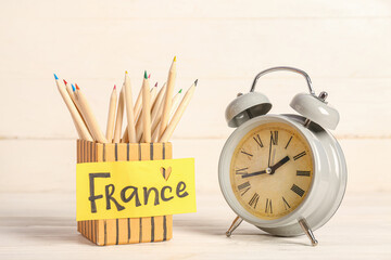 Holder with color pencils, word FRANCE and alarm clock on light wooden background