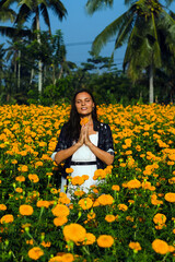 Obraz na płótnie Canvas A young girl, brunette, folds her hands in namaste, meditates and thanks God, in a beautiful flower field.
