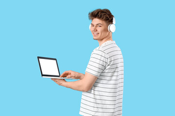 Young man in headphones using laptop on blue background