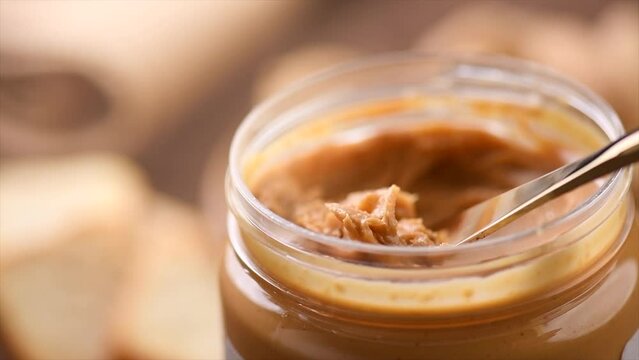Peanut butter in a glass jar. Creamy smooth peanut butter. Mixing with a knife, making sandwich, organic food. American cuisine. Slow motion 