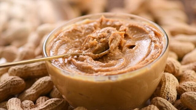 Peanut butter in a glass jar. Creamy smooth peanut butter. Mixing with a spoon, making sandwich, organic food. American cuisine. Slow motion