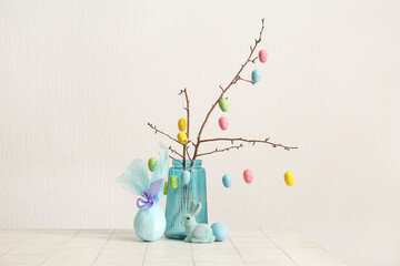 Branches with Easter color eggs in blue vase, gift egg and rabbit on white background