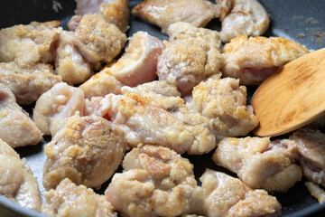 鶏肉(片栗粉をまぶした鶏モモ肉)をフライパンで炒める調理シーン。
