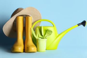 Composition with watering can, rubber boots and hat on blue background. Garden tools