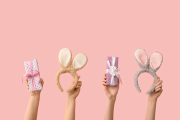 Female hands with gifts and Easter bunny ears headbands on pink background
