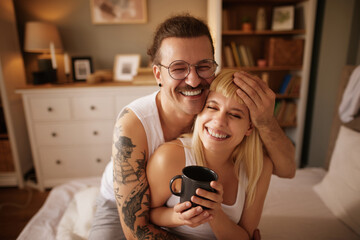 Tattooed man and his beautiful wife enjoying coffee in bed