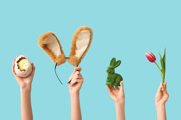 Female hands with rabbit, chick, bunny ears headband and tulip on blue background. Easter concept.