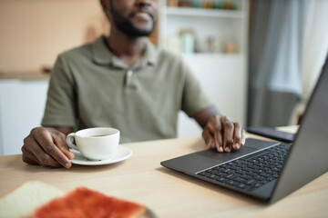 Close up of African American man using laptop and working at kitchen table during breakfast copy space