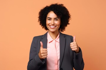 
Photograph of a confident biracial businesswoman in her early 30s, against a soft peach background, smiling brightly and showing a thumbs-up gesture - Powered by Adobe