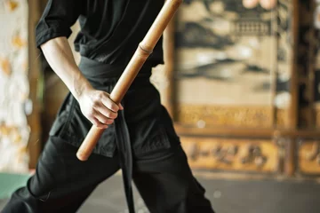 Fototapete person in black kung fu attire practicing with a wooden staff in a gym © studioworkstock