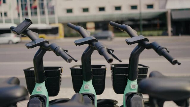 Closeup on bicycle handlebar standing on street near city road. Bike rent station outdoors near city center and road with traffic cars on background. Ecological transport