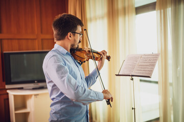 Man playing violin at home. He is practicing for live performance.