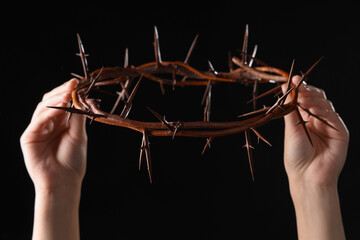 Female hands with crown of thorns on black background. Good Friday concept