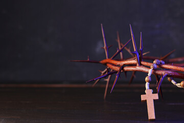 Crown of thorns and beads with cross on wooden table against black grunge background, closeup. Good Friday concept